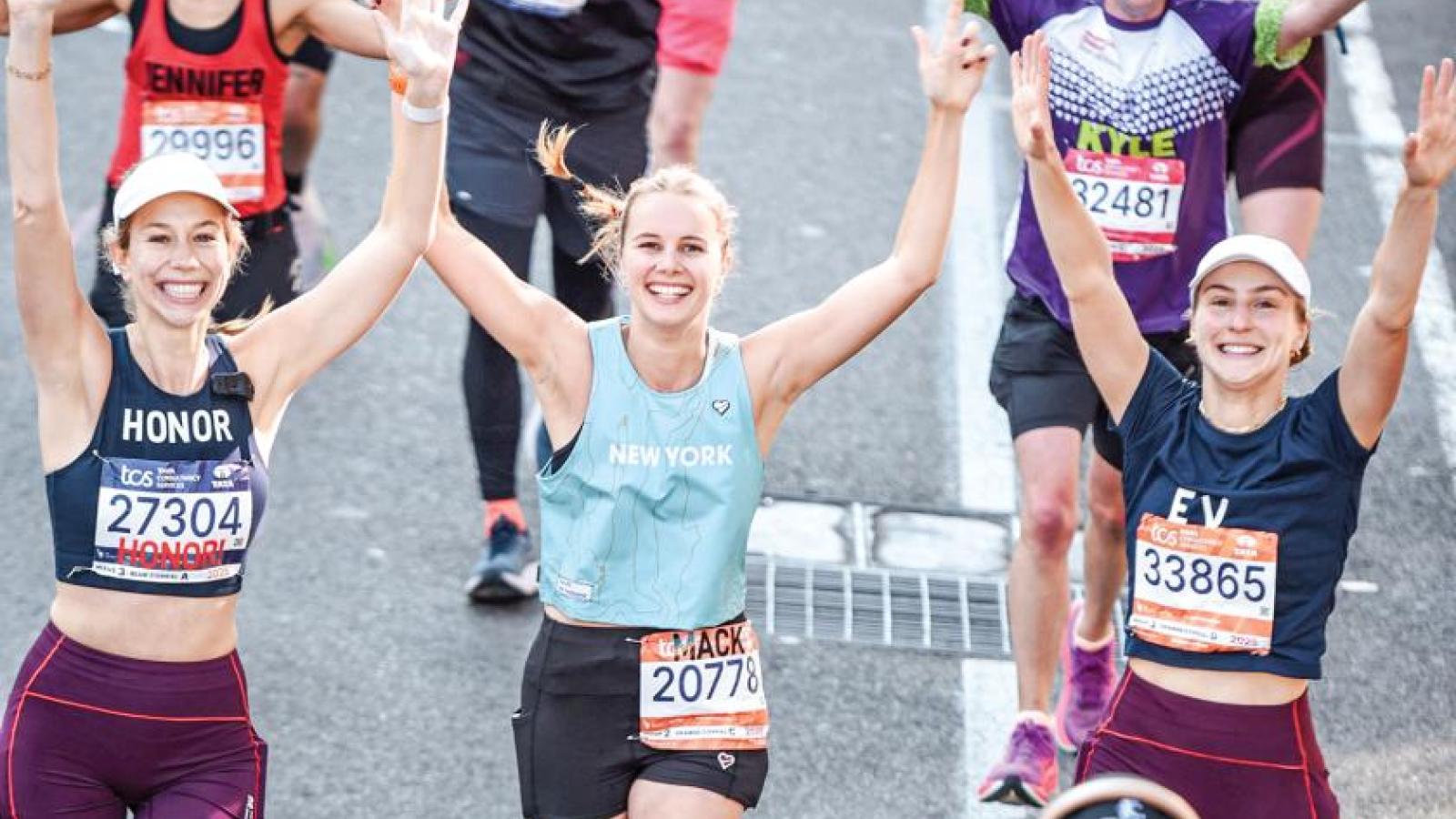 People running a race smile at the camera with their arms up in celebration