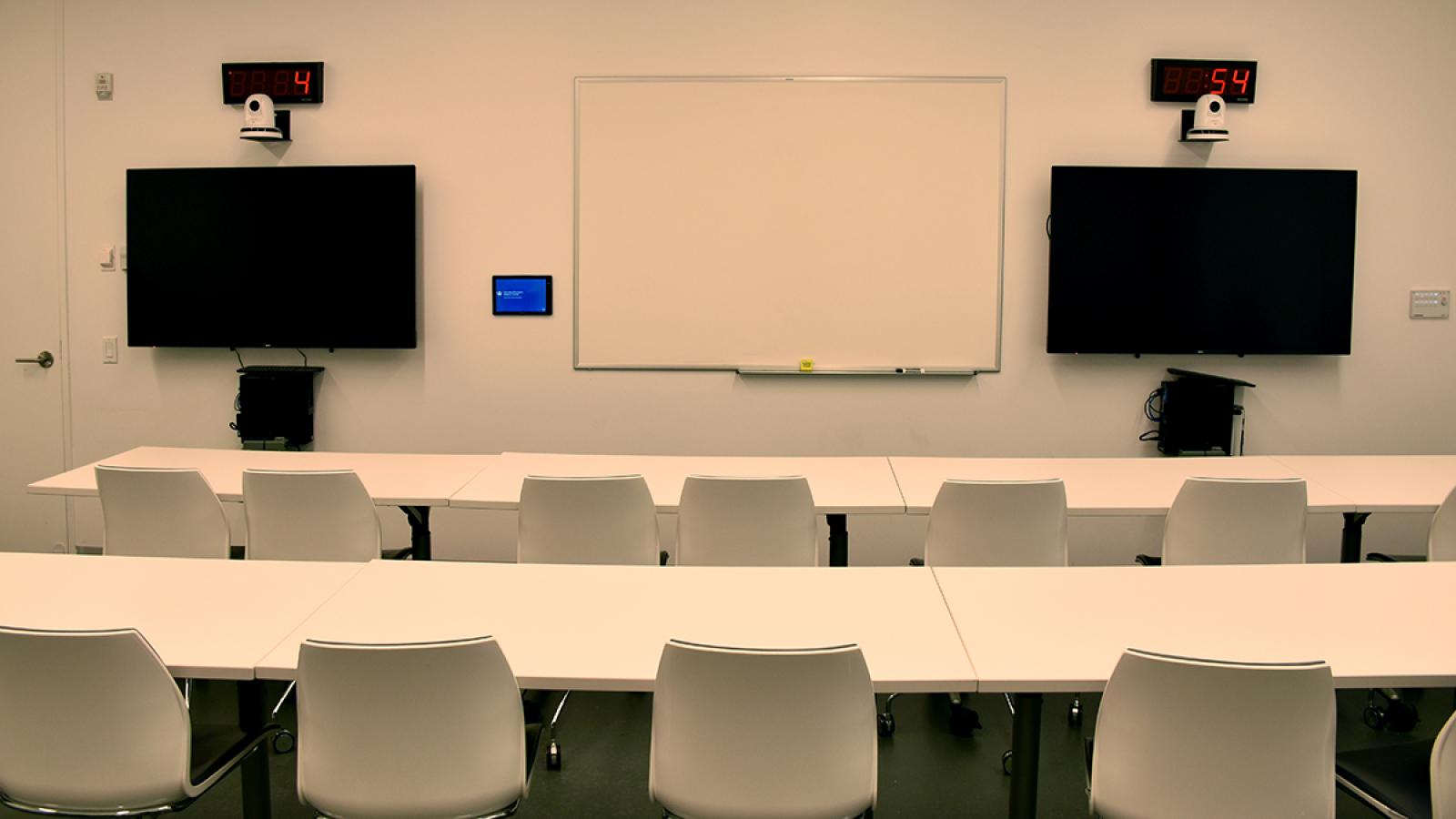 Conference room equipped with rows of large tables and chairs, monitors, PCs, and web cameras.