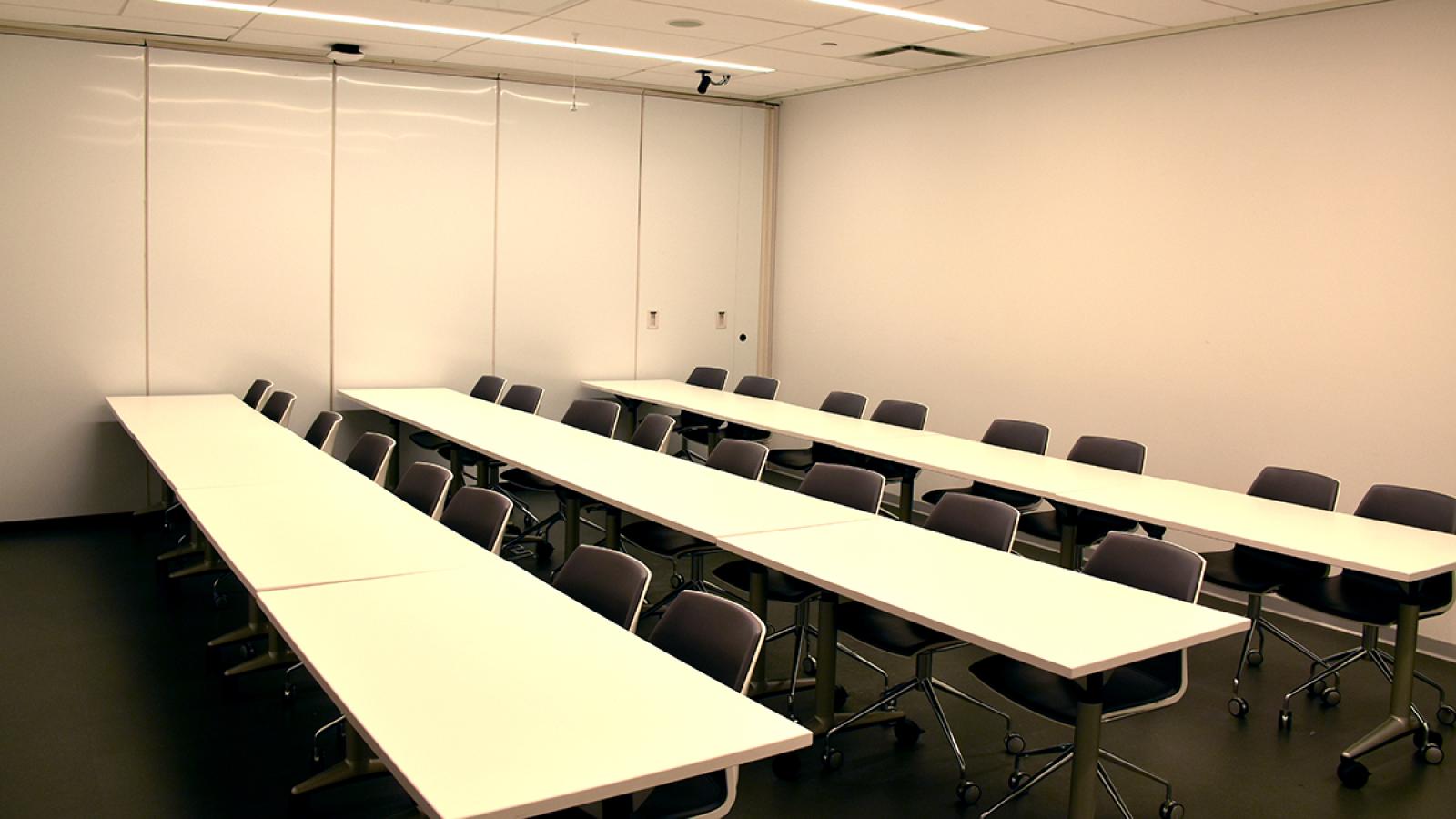 Conference room equipped with rows of large tables and chairs, monitors, PCs, and web cameras.