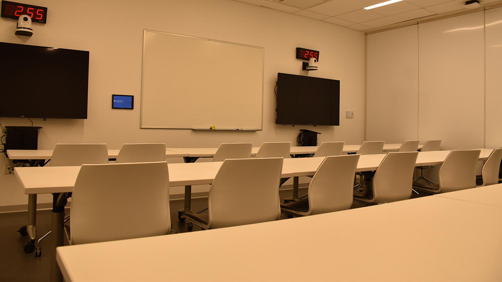 Conference room equipped with rows of large tables and chairs, monitors, PCs, and web cameras.