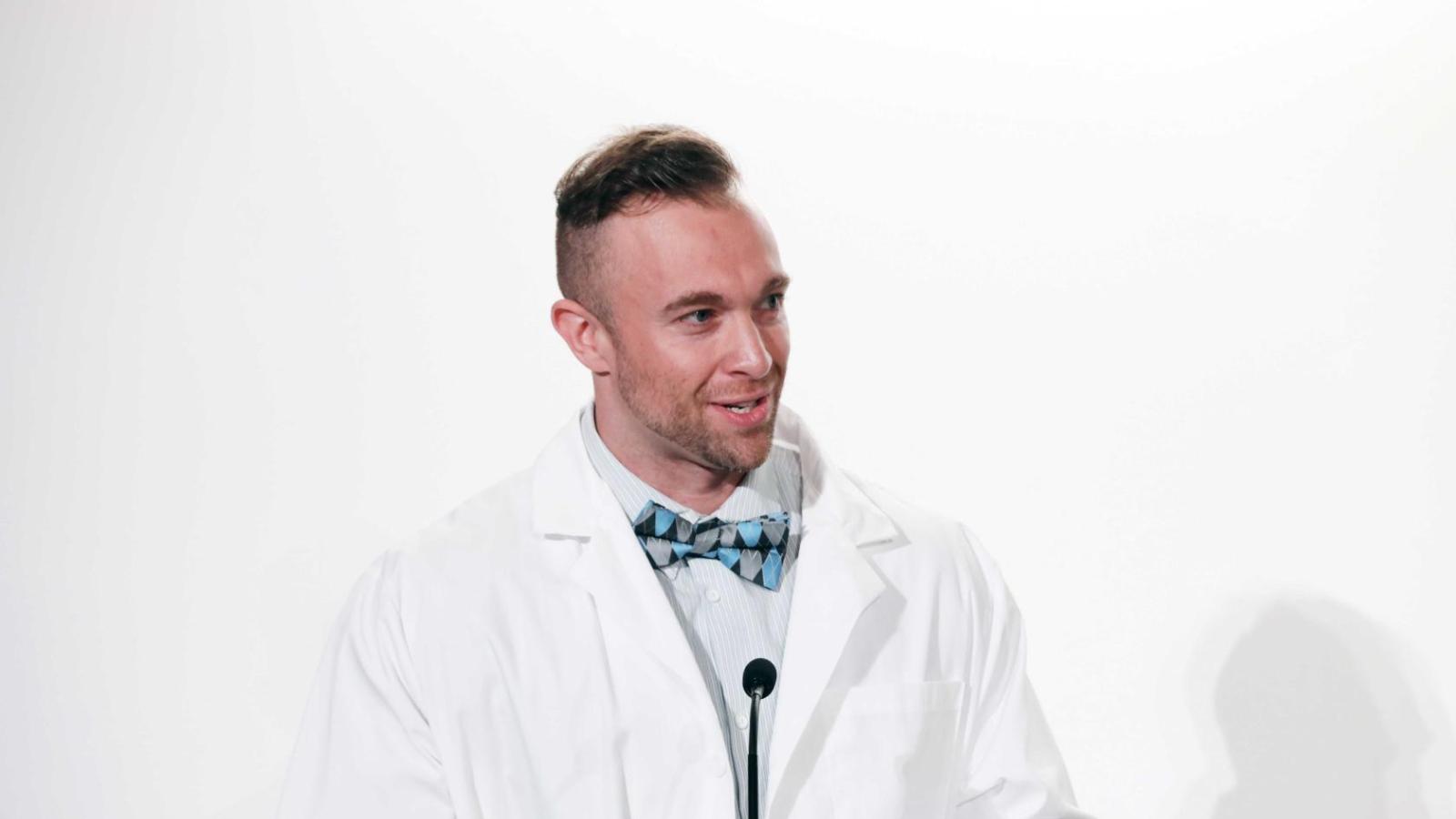 Alumnus in a white coat speaks at a podium during a Columbia University white coat ceremony.