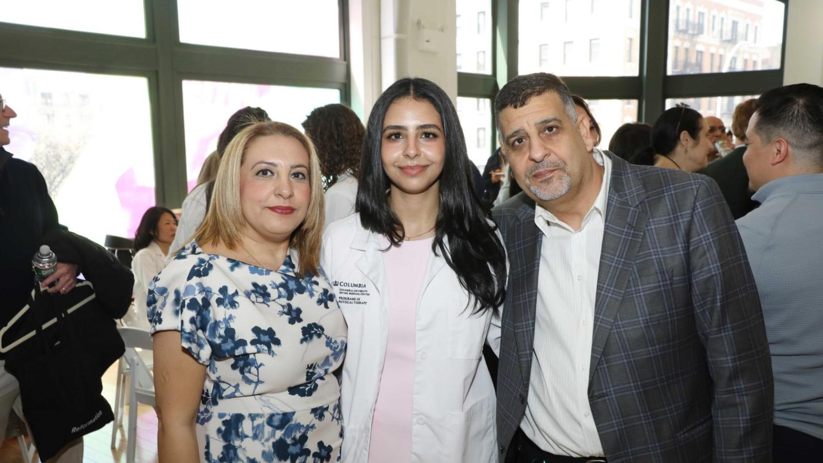 Columbia physical therapy student in a white coat poses with family members during the white coat ceremony reception.