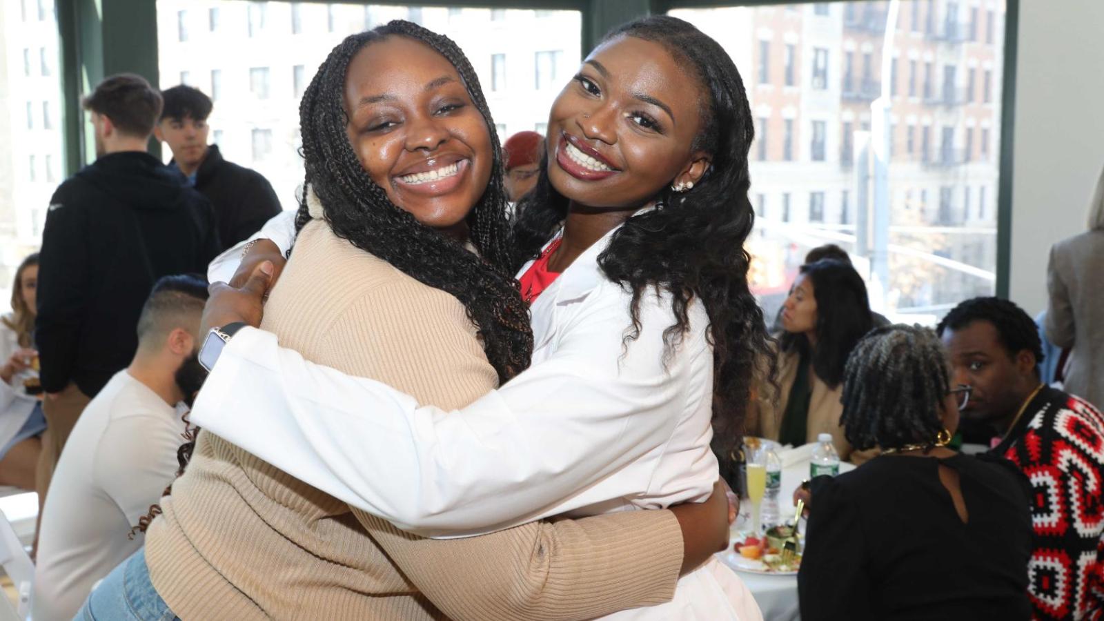 Columbia physical therapy students, including one in a white coat, share a hug during the white coat ceremony reception.