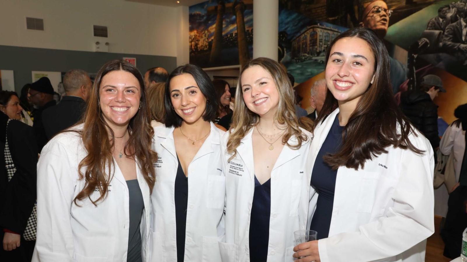 Four Columbia physical therapy students in white coats smile together during the white coat ceremony reception.