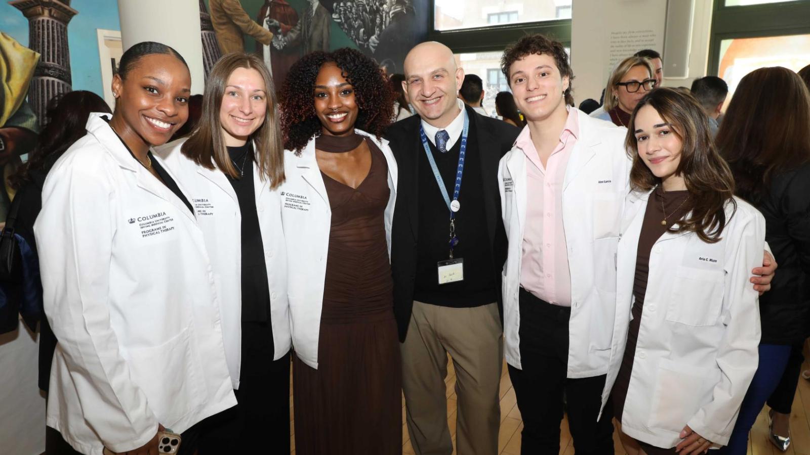 Columbia physical therapy students in white coats pose with a faculty member during the white coat ceremony reception.