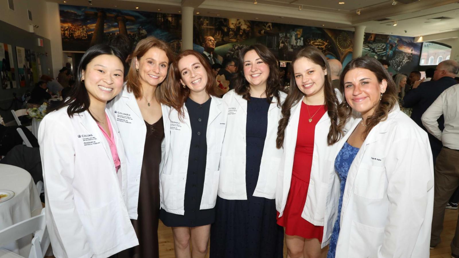 Columbia physical therapy students in white coats pose together at the white coat ceremony reception.