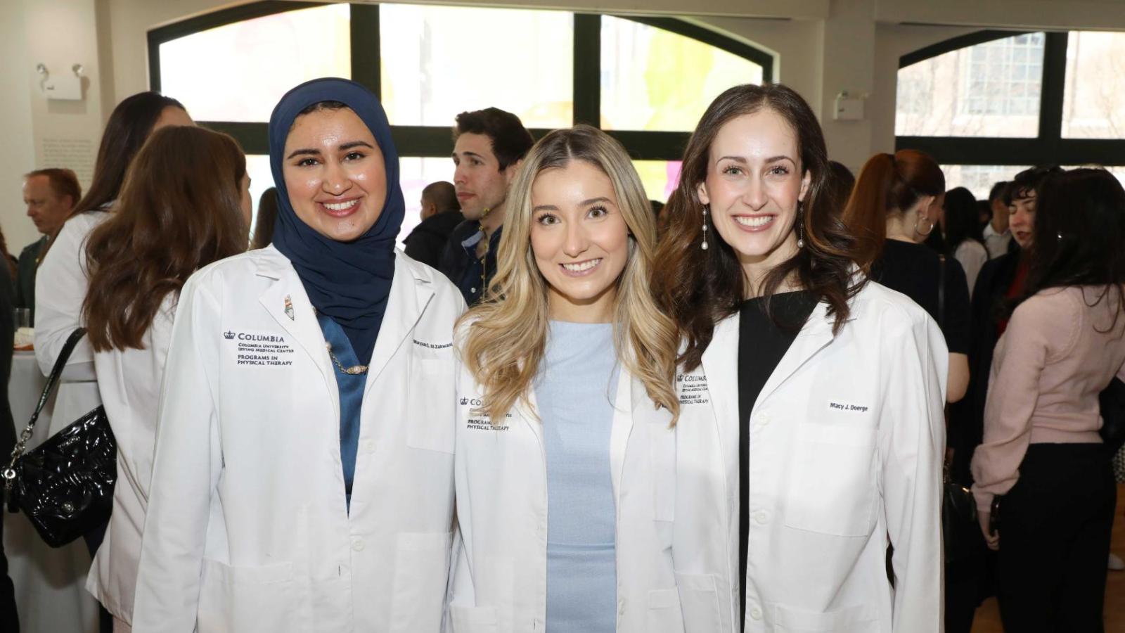Columbia physical therapy students in white coats pose together at the white coat ceremony reception.