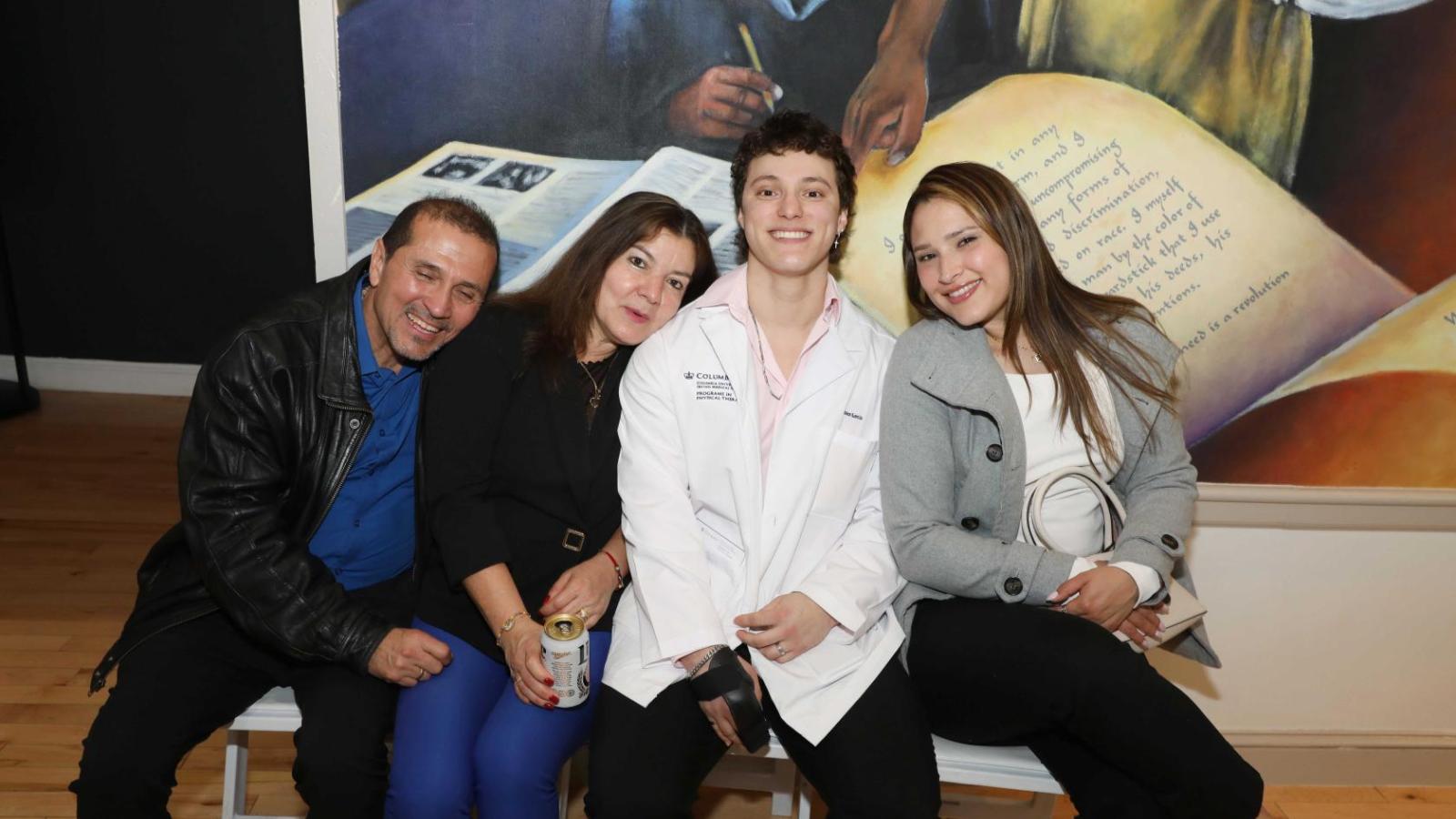 Columbia physical therapy student in a white coat sits with family members during the white coat ceremony reception.