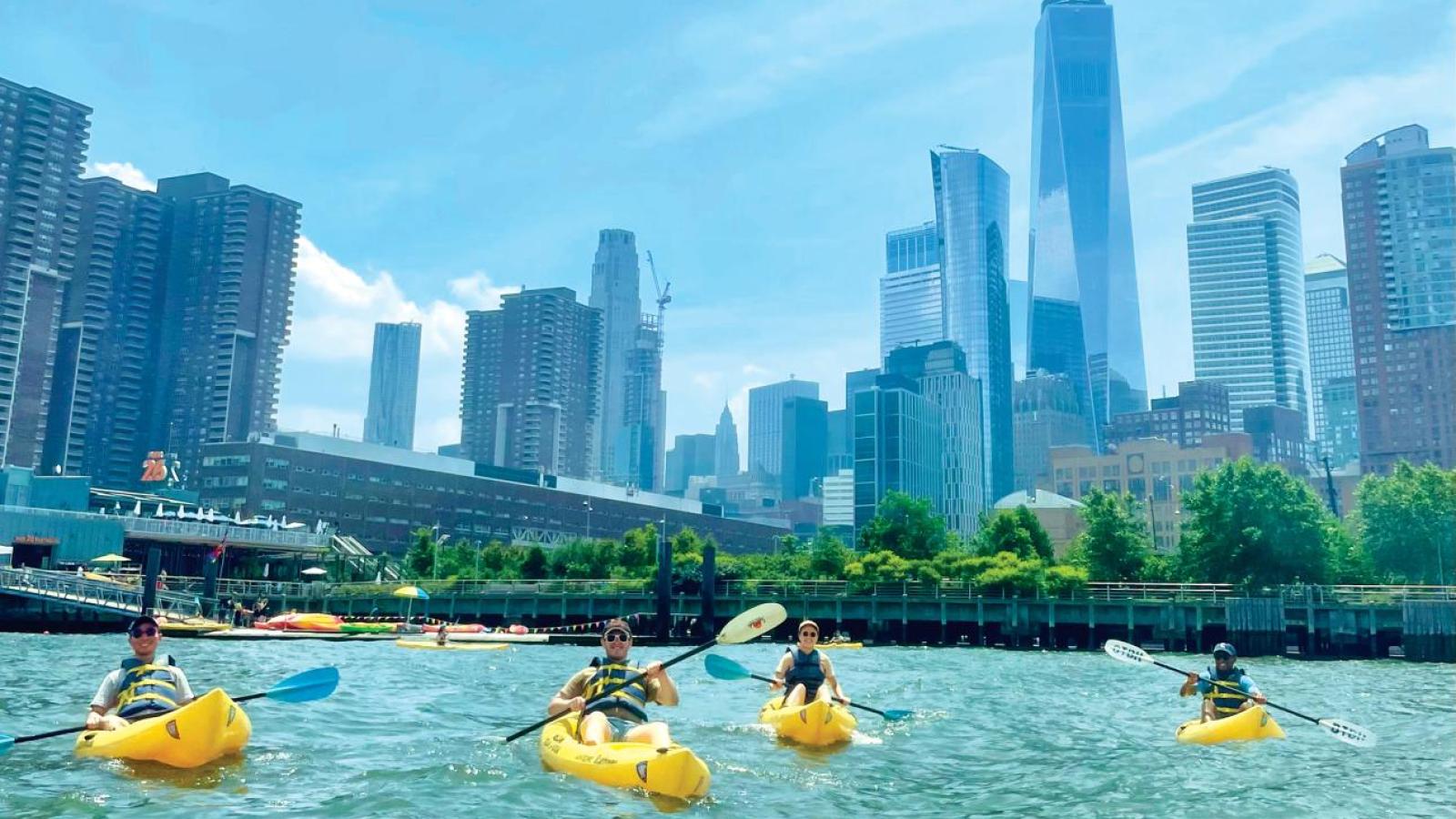 People in yellow kayaks float in front of the Manhattan skyline