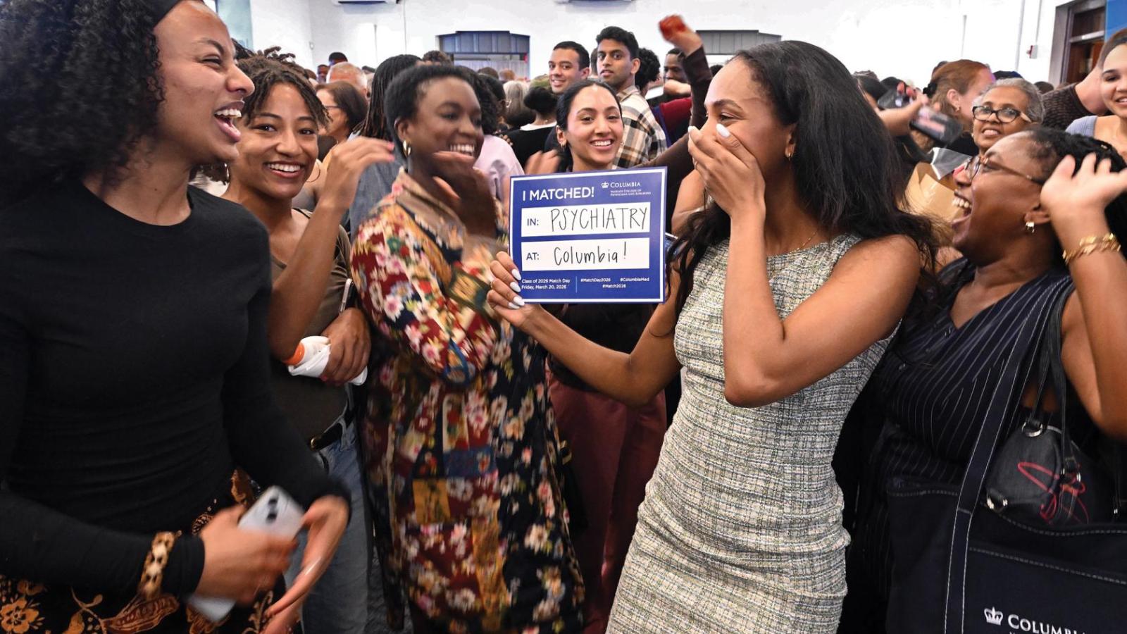 A woman holds a blue sign that says Columbia Psychiatry while her family cheers around her