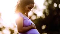 Smiling pregnant woman rests hand on her belly.