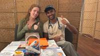 Two students at a Q Clinic outreach table give thumbs up while sharing health resources.