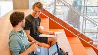 Two Columbia medical students have a conversation while sitting on the orange staircase in the Vagelos Education Center.