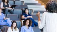 A faculty member giving a lecture to a class of students wearing scrubs.