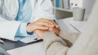 A doctor talking with the patient while holding their hands.
