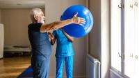 Senior man exercising with a physiotherapist using fitness ball.