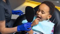 Young boy touches tooth with filling and looks in mirror during dental appointment.