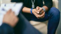 Patient sits with hands clasped, across from therapist during session.