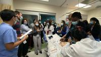 Pediatric residents watch demonstration with manikin in hospital bed.