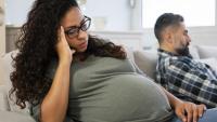 A pregnant women thinking on a couch with her husband in the background