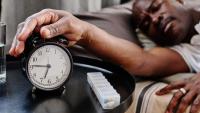 man sleeping with hand on alarm clock
