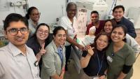 Group of healthcare staff posing for a photo around a medical training mannequin in a clinical simulation room.