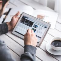 A man reads a tablet and enjoys a coffee.