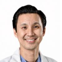 An image of Dr. Chang smiling, wearing his lab coat and blue scrubs.